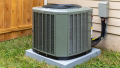 Outdoor HVAC unit installed on a concrete base beside a wooden fence, surrounded by grass, illustrating air conditioning maintenance and installation services relevant to Precision Air in West Chester, Pennsylvania.