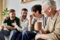 Group of four people laughing and enjoying a cozy gathering, sharing drinks in a comfortable living room setting, reflecting family warmth and connection.