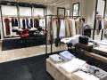Minimalistic retail clothing shop interior with neatly arranged garments on racks and tables, emphasizing a comfortable shopping environment for customers.