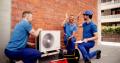 HVAC technicians in blue uniforms collaborating on air conditioning unit installation, emphasizing teamwork and expertise in residential HVAC services for Precision Air in Berwyn.