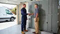 HVAC technician in uniform shaking hands with a homeowner in a garage, emphasizing professional service and customer satisfaction for emergency HVAC repairs.