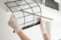 Woman wearing gloves cleaning an air conditioner filter to improve indoor air quality, emphasizing Precision Air Heating & Cooling's focus on healthier home environments.