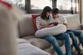 Couple sitting on a couch in a cozy living room, smiling and bonding while holding a baby, emphasizing family moments and comfort in a home setting.