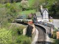 Historic Berwyn Train Station with vintage trains, passengers waiting, and lush greenery surrounding the area.