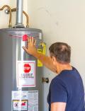 Adult male inspecting newly installed water heater with performance label and warning sign in residential setting.