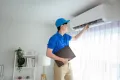 Technician in blue uniform adjusting air conditioner indoors, emphasizing expert AC repair services by Precision Air Heating & Cooling in a residential setting.