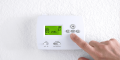 Thermostat displaying indoor temperature of 65°F with a hand adjusting settings, relevant to blog topics on thermostat use and energy efficiency.