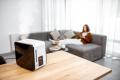 Woman relaxing on a couch while using a smartphone, with a modern humidifier emitting steam on a wooden table, illustrating indoor air quality improvement in a comfortable living space.