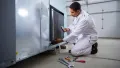 HVAC technician performing maintenance on a cooling unit, using tools and equipment for inspection in a residential setting, emphasizing the importance of regular HVAC care for efficiency and air quality.