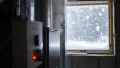 Heating system emitting steam with a red indicator light, snow visible through a window, illustrating HVAC issues in winter conditions.