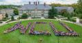 Large group of people forming "VCU" on a grassy area in front of a historic building, showcasing community spirit at West Chester University.