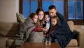 Family huddled together under blankets, using a smartphone to stay connected during a winter storm, emphasizing the importance of comfort and safety in home environments.