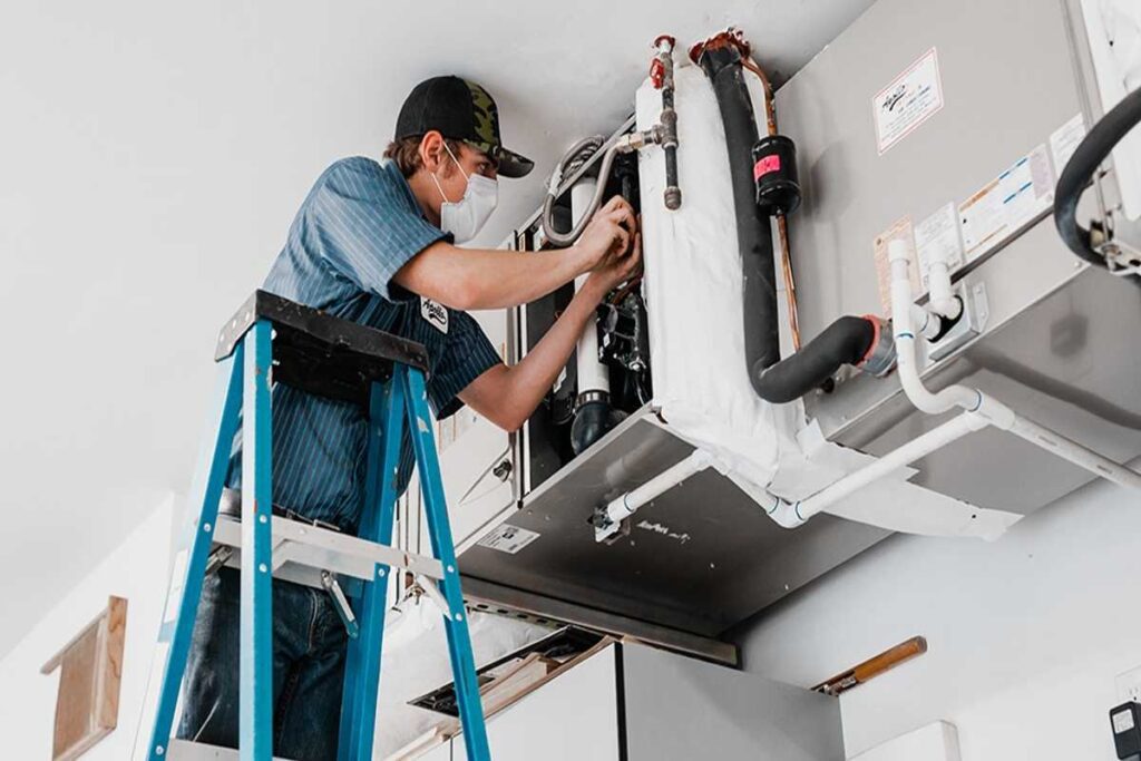 HVAC technician performing maintenance on air conditioning unit while using a ladder, emphasizing Precision Air Heating & Cooling's commitment to reliable service in Concordville, PA.