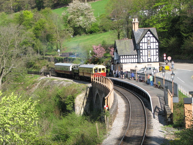 Historic Berwyn Train Station with vintage trains, passengers waiting, and lush greenery surrounding the area.