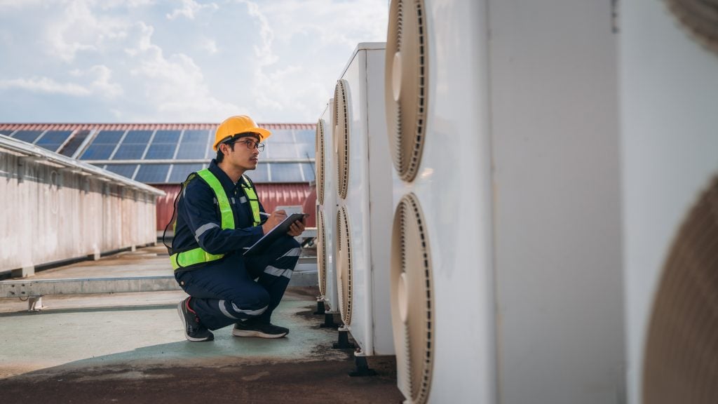 HVAC technician in safety gear inspecting air conditioning units on a rooftop, emphasizing Precision Air's commitment to expert HVAC services and maintenance in Paoli.