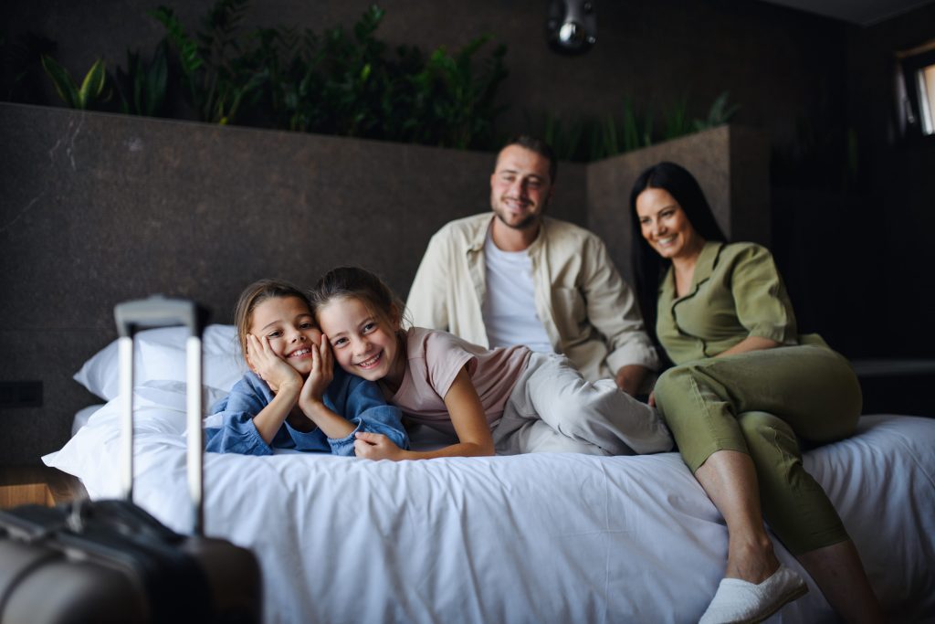 Happy family of four in West Chester, PA, enjoying their vacation. Parents and two daughters smiling on a cozy bed, ready for Furnace Repair.