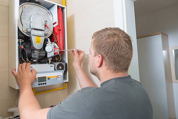 Man performing furnace repair with a screwdriver on a wall-mounted unit. Ensure optimal heating with professional maintenance services.