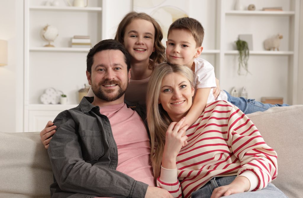 Happy family of four, including parents and two children, sitting together on a sofa in a cozy living room, showcasing warmth and comfort, reflecting the importance of home and family in maintaining a comfortable environment.